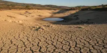 Paisaje árido y agrietado por la sequía en España, con un embalse casi vacío al fondo.