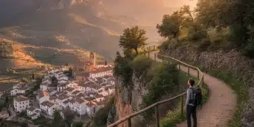 Senderista contemplando un pueblo histórico español entre montañas al atardecer.